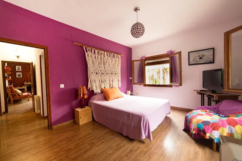 Dormitorio con pared magenta, cama de matrimonio y cabecero de macramé