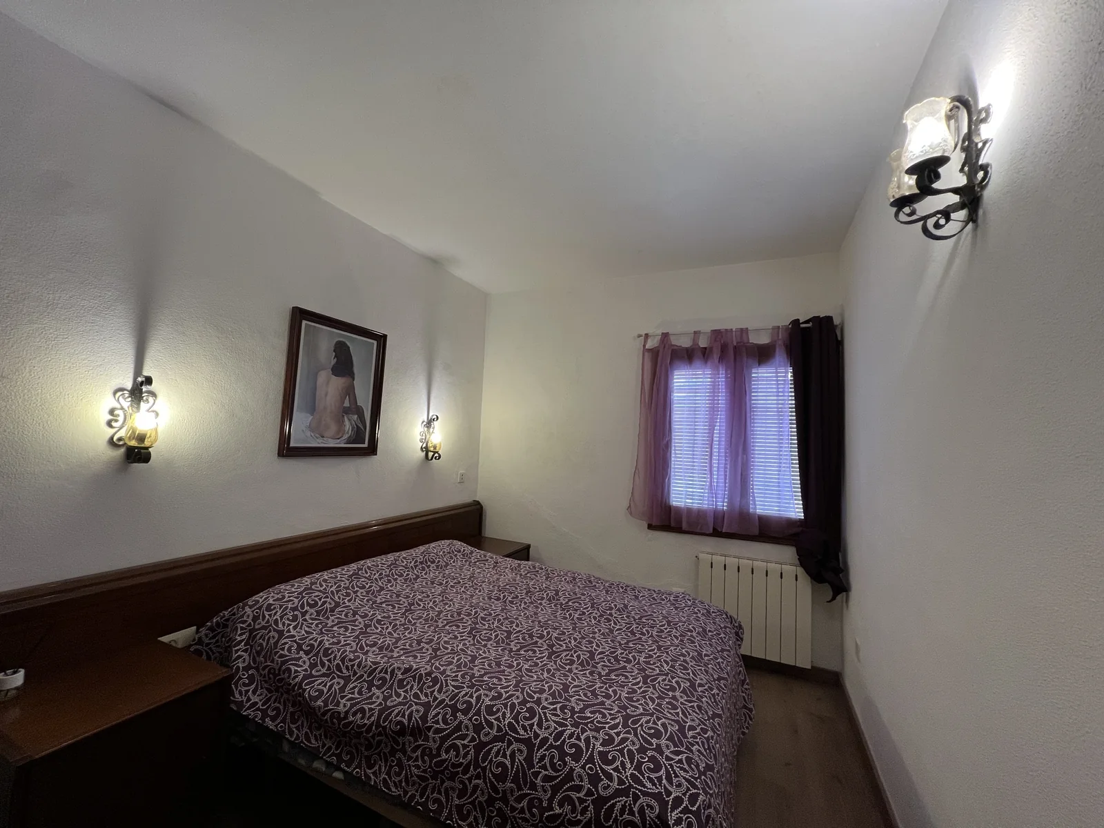 Dormitorio con cabecero de madera oscura, colcha estampada y apliques de pared