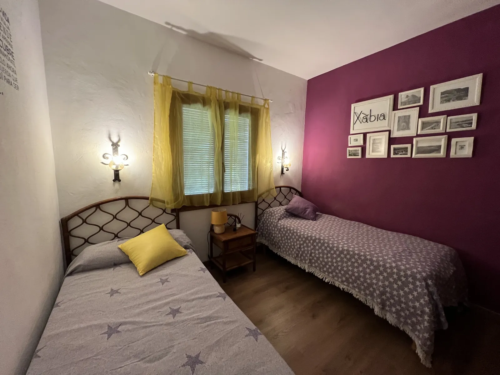 Dormitorio con dos camas individuales y pared malva con fotografías de Xàbia
