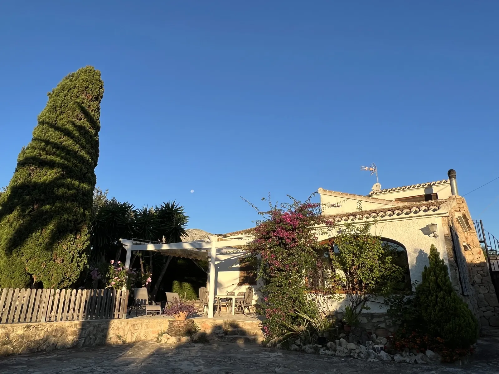 Fachada de la casa con el ciprés y la luna en la luz de la tarde